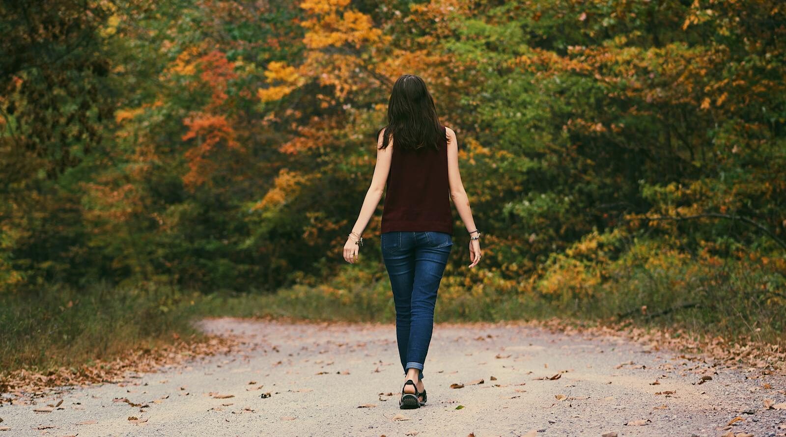 Woman in Brown Sleeveless Dress and Blue Jeans Standing on Gray Path Road